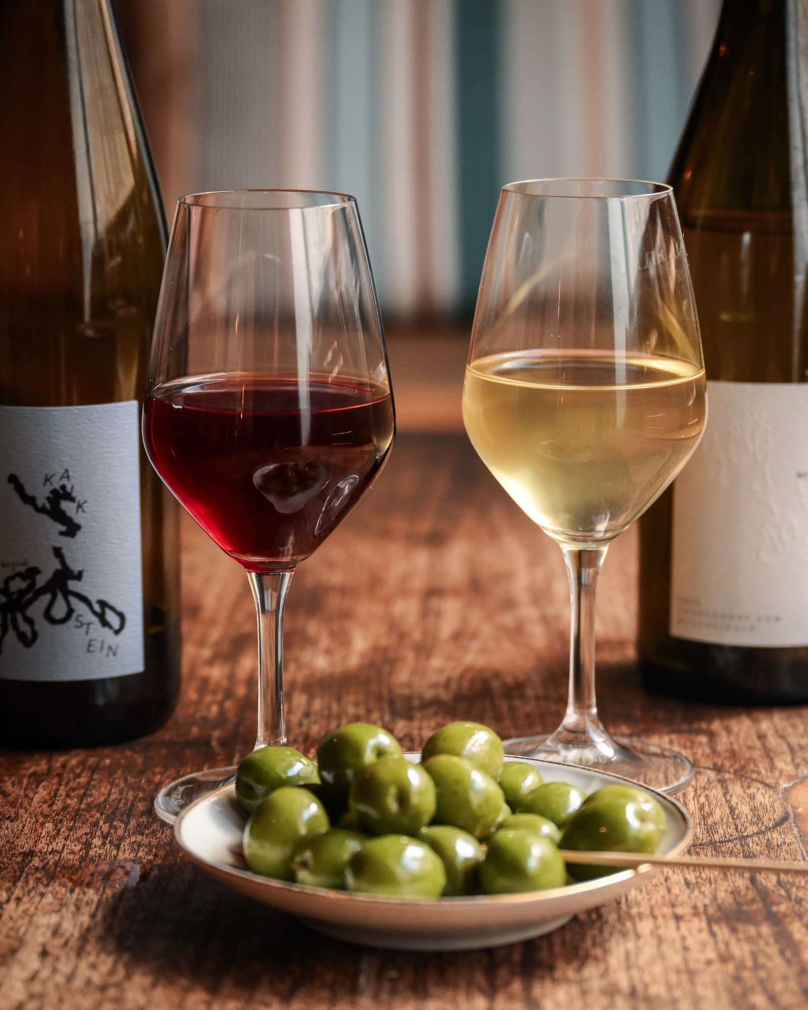 A glass of red and a glass of white on the table with a bowl of olives between them